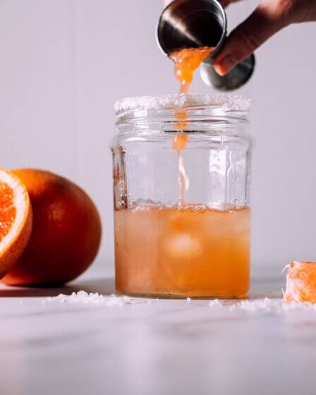 person pours liquid on jar near orange fruits