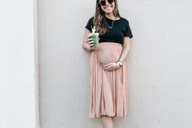 woman in black t-shirt and pink skirt standing beside wall