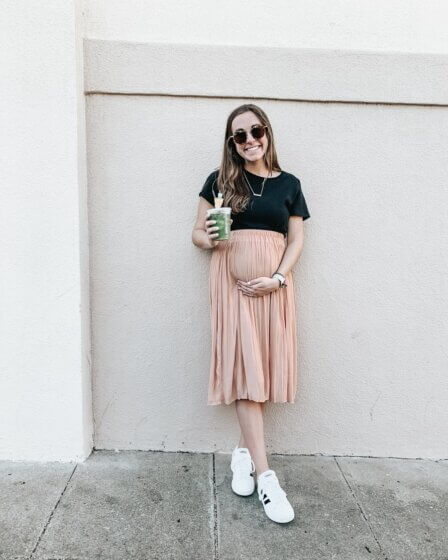 woman in black t-shirt and pink skirt standing beside wall